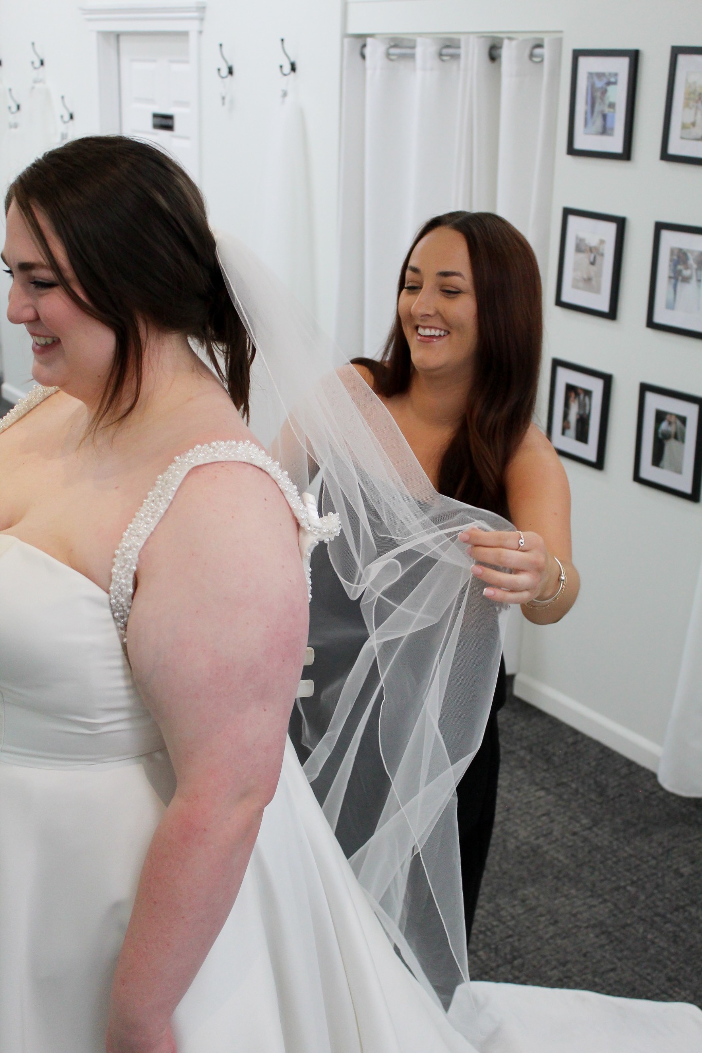 A smiling bridal stylist arranging a bride’s veil during her appointment